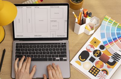 Diseñadora gráfica trabajando en formatos de piezas publicitarias en su notebook, junto a un muestrario de colores impreso